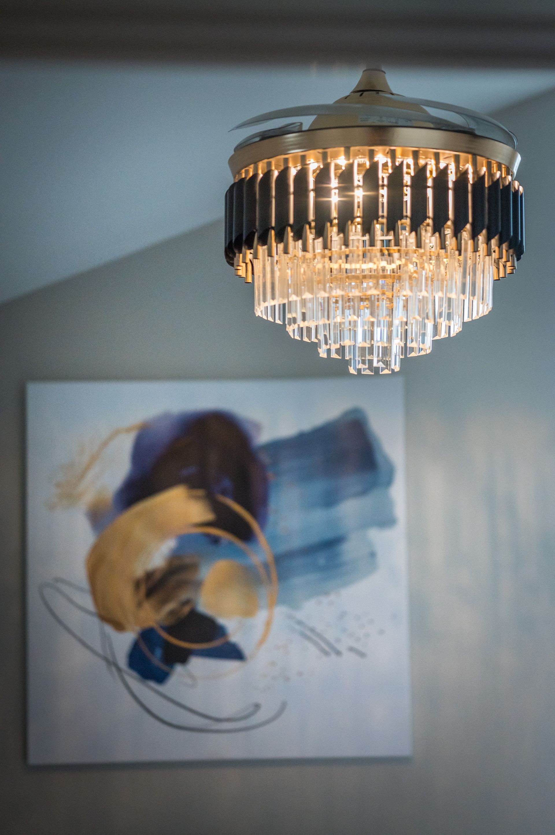 Crystal chandelier ceiling fan, over abstract blue and gold artwork on a white wall.