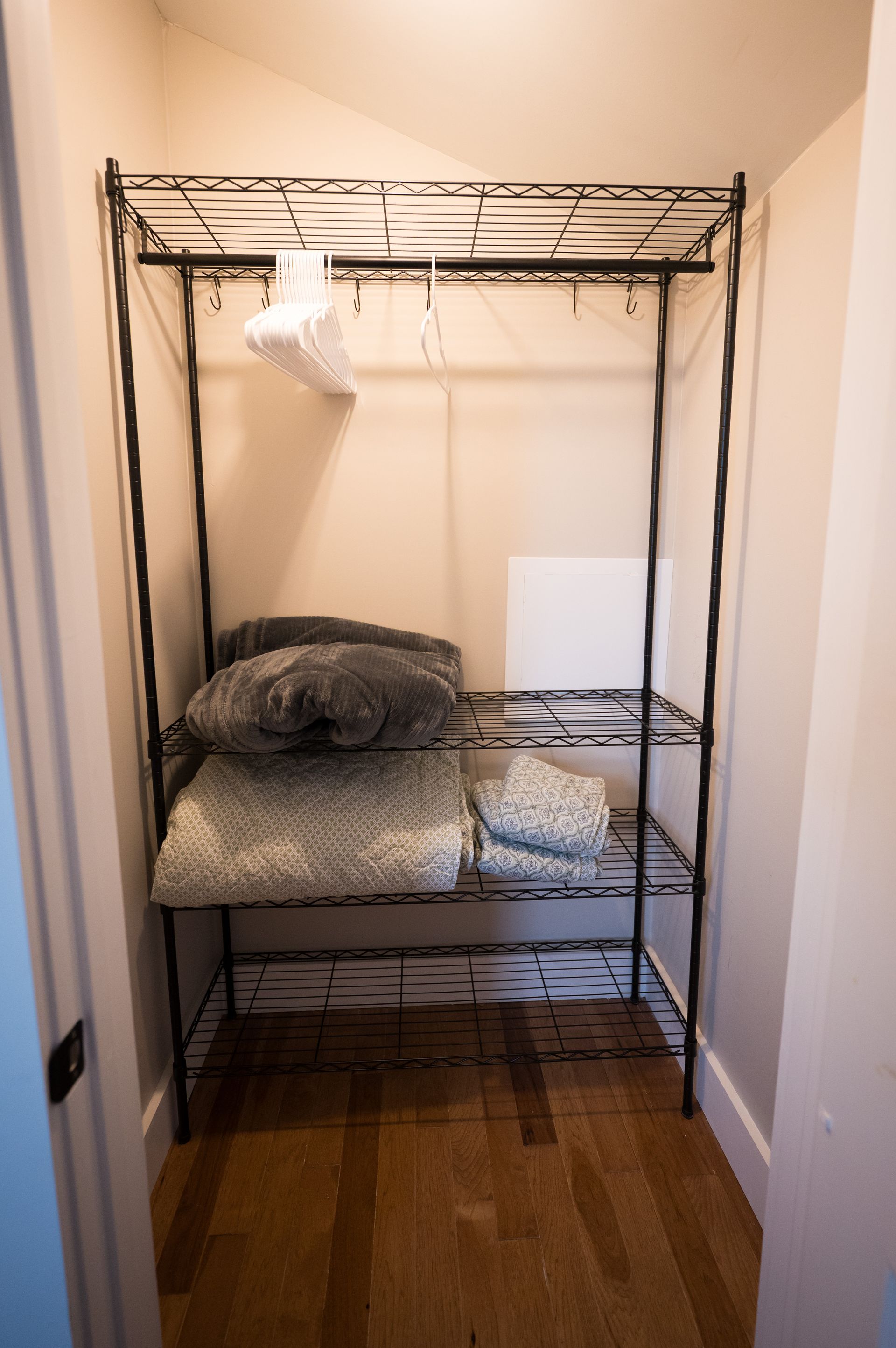 Black wire shelving unit in a closet holding blankets and clothes hangers.