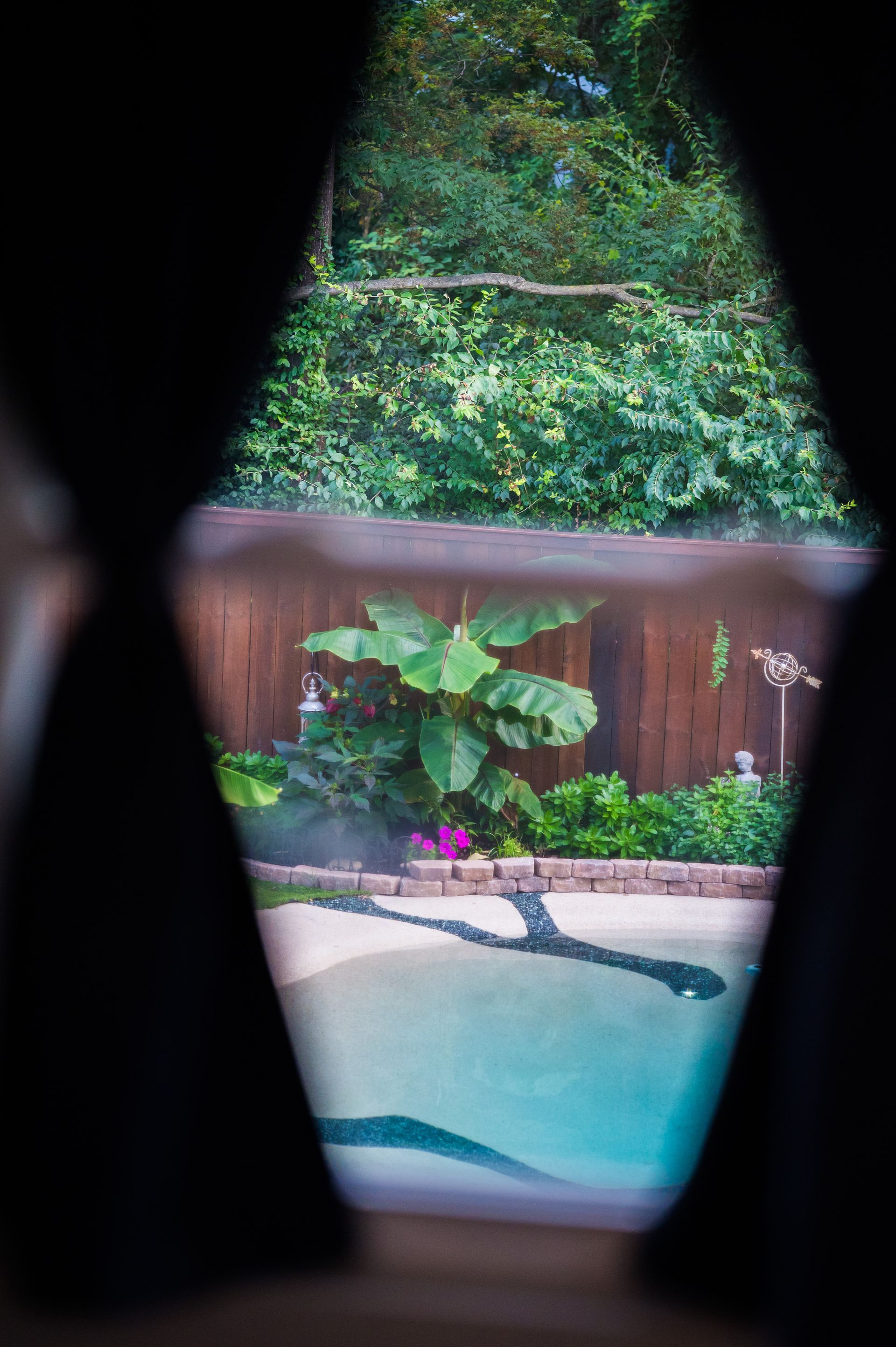 View of a backyard pool and garden through a diamond-shaped opening.