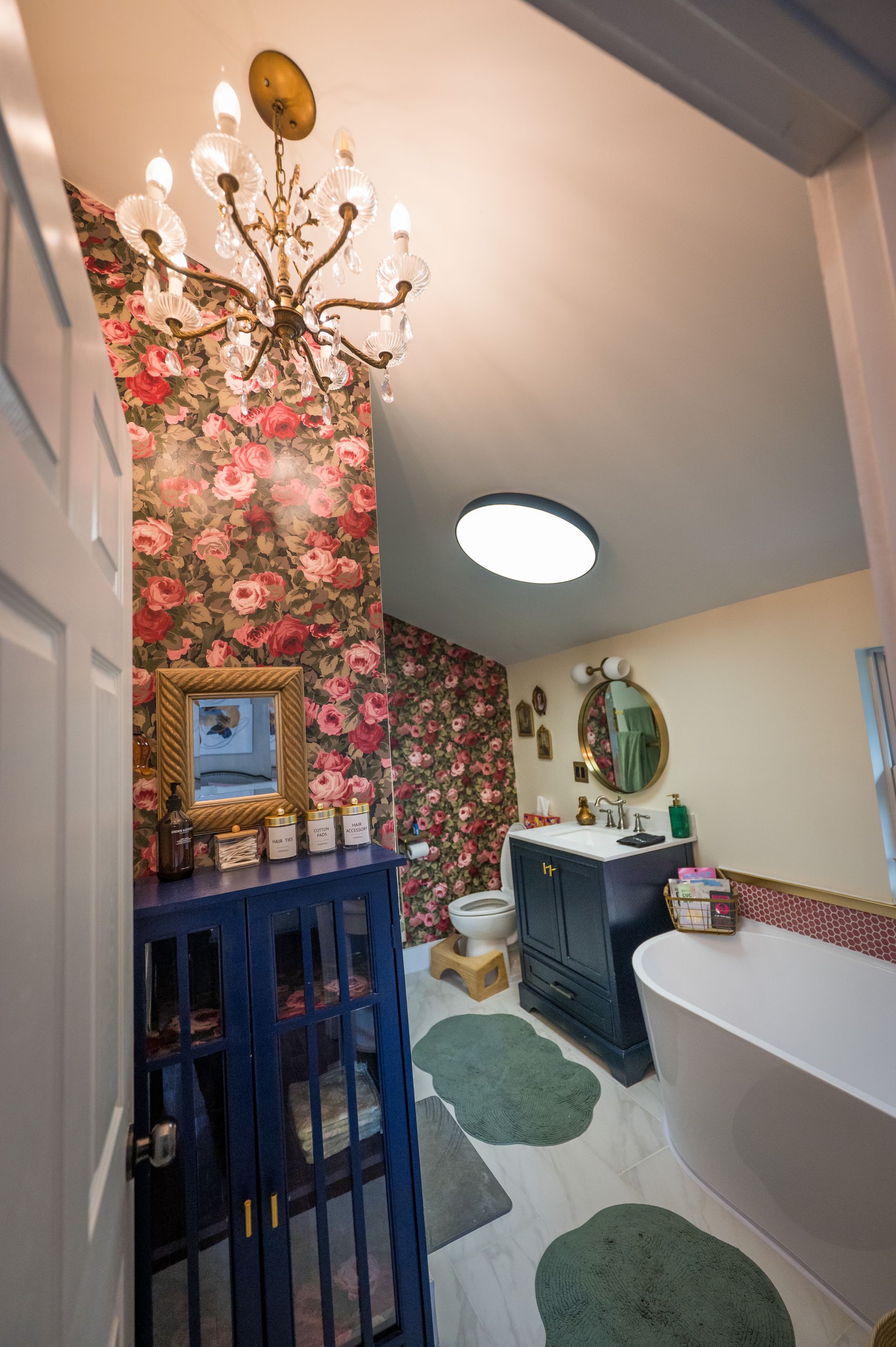 Bathroom with floral wallpaper, blue cabinet, chandelier, and a white soaking tub.