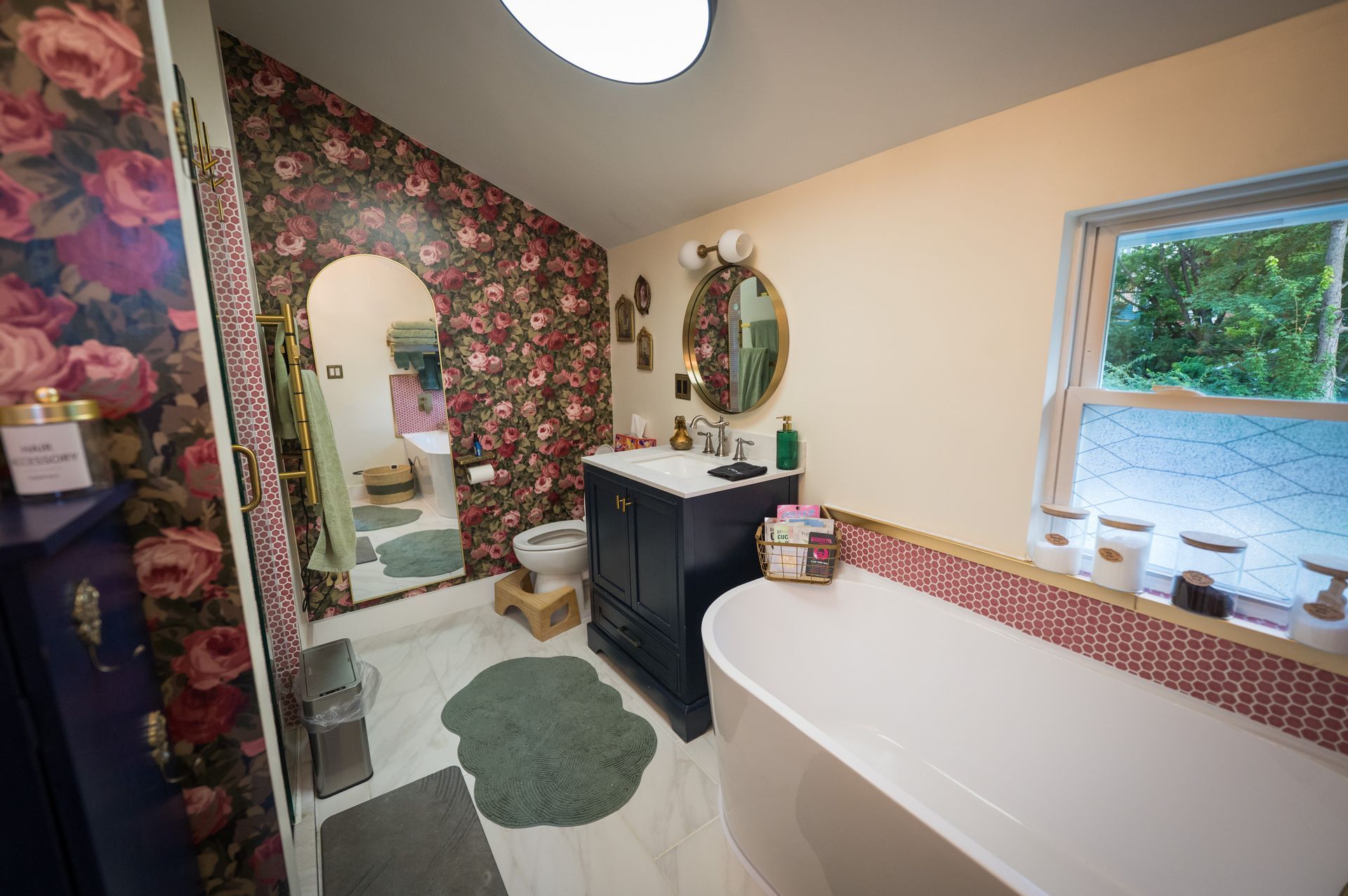 Bathroom with floral wallpaper, a white bathtub, and a dark blue vanity.