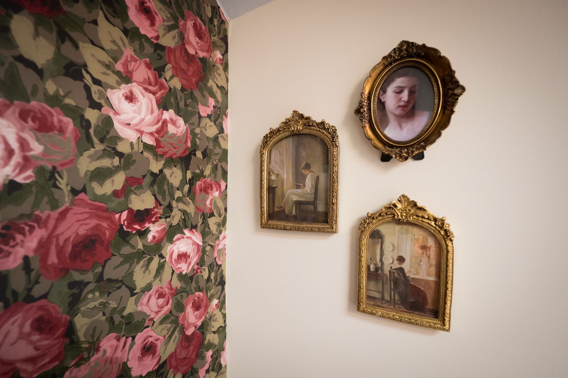 Wall with three framed antique paintings and a floral curtain.
