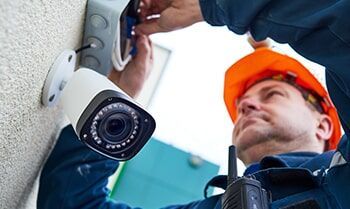 A Man is Installing a Security Camera on a wall — Electronic Security in Tweed, NSW
