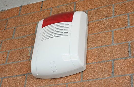 A White and red Alarm is Mounted on a Brick wall — Electronic Security in Tweed, NSW