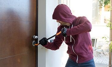 A Man in a Hoodie is Breaking into a House with a Crowbar — Electronic Security in Tweed, NSW