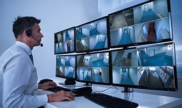 A Man is Sitting at a Desk Looking at a Bunch of Monitors.
