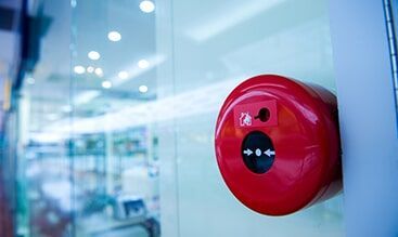 A Red fire Alarm is Sitting on a Glass door — Electronic Security in Tweed, NSW