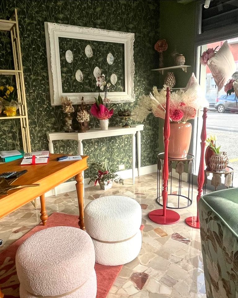 Una stanza con un tavolo, sedie, pouf e fiori sul muro.