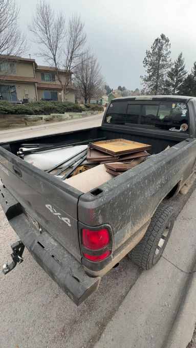 Dark pickup truck bed filled with materials, parked on a paved road.