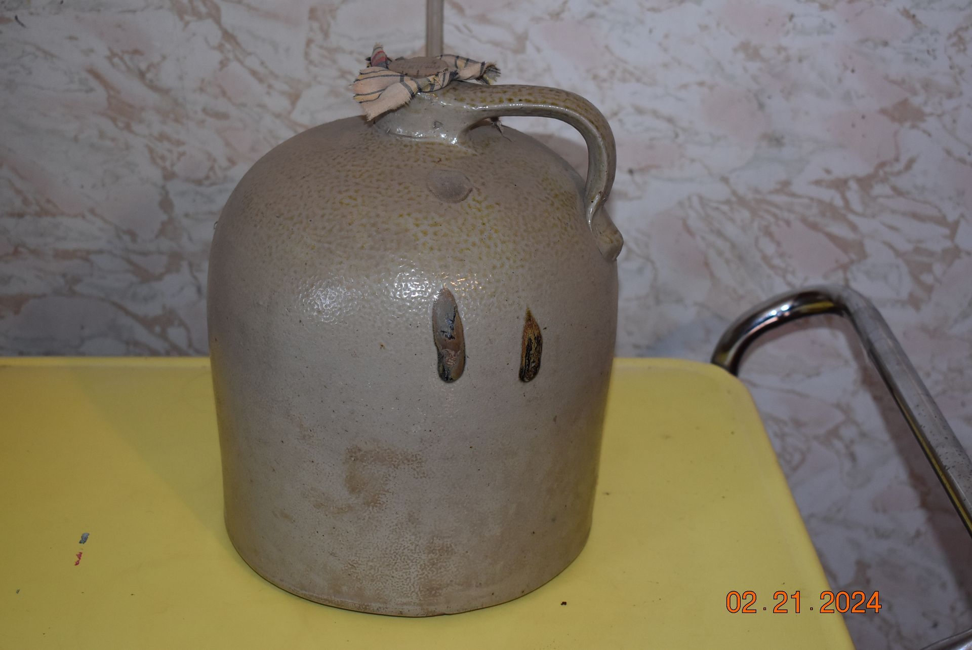 An old antique gray bottled jug with a handle is sitting on a yellow table.
