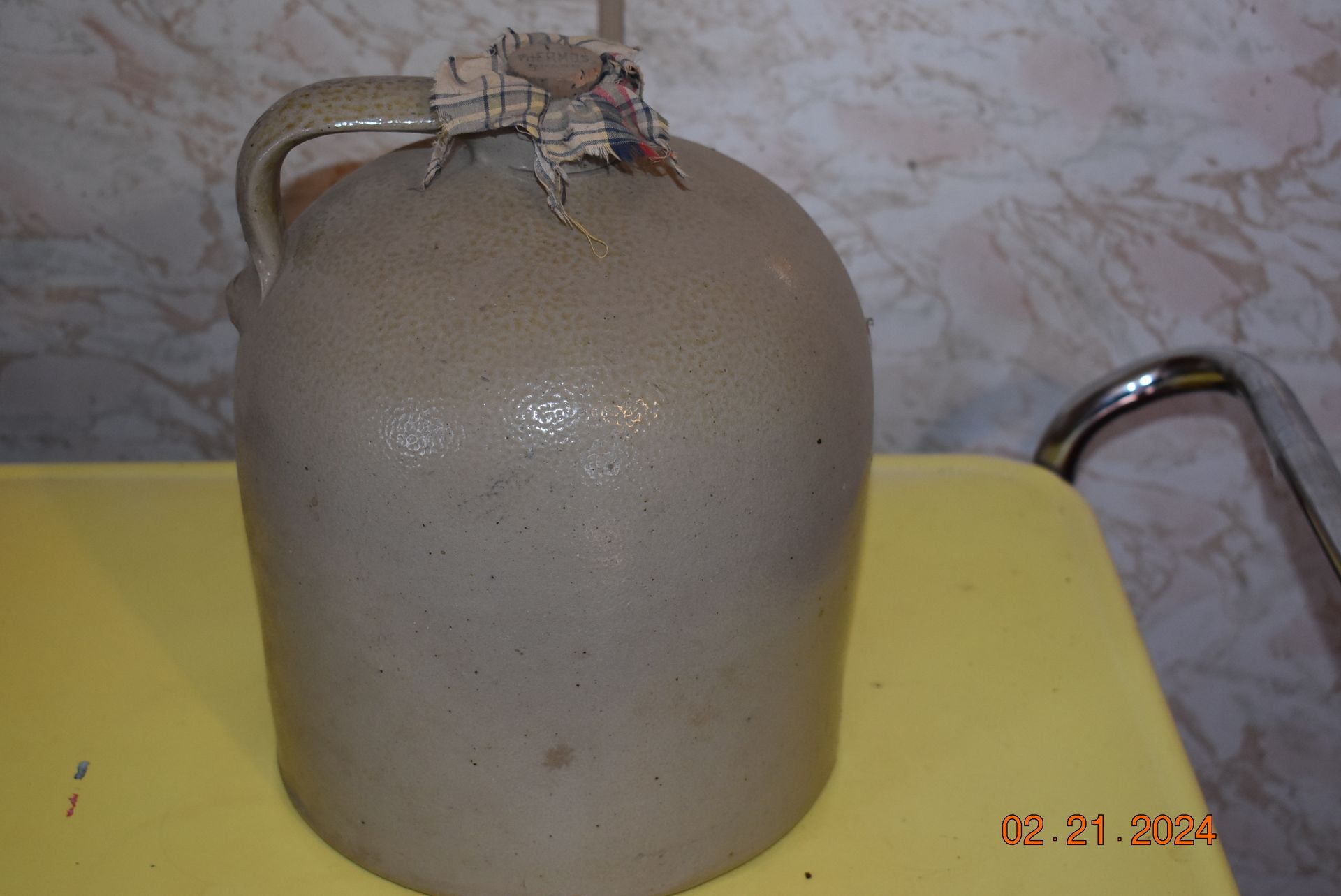 An old antique gray bottled jug with a handle is sitting on a yellow table.