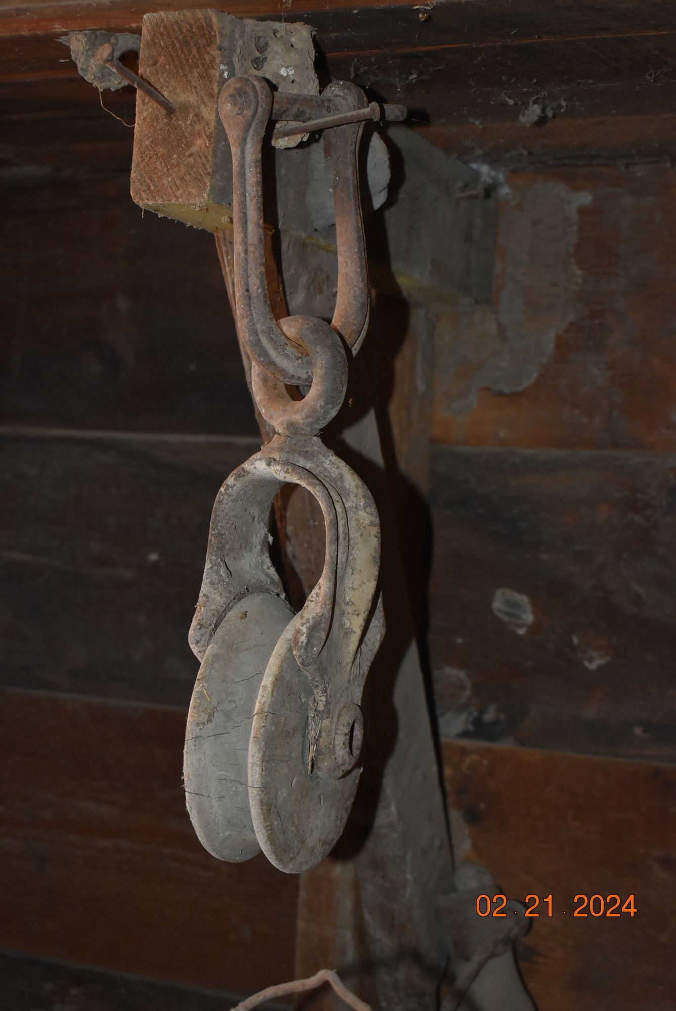 Antique rope pulley hanging from a wooden wall.