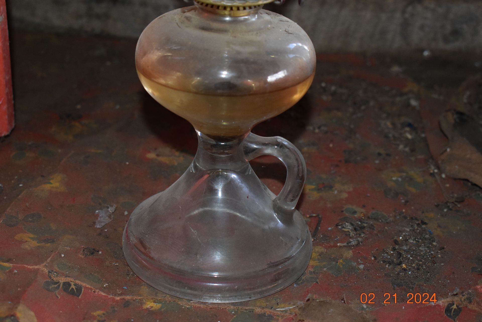 a clear glass oil lamp with a handle is sitting on a table .