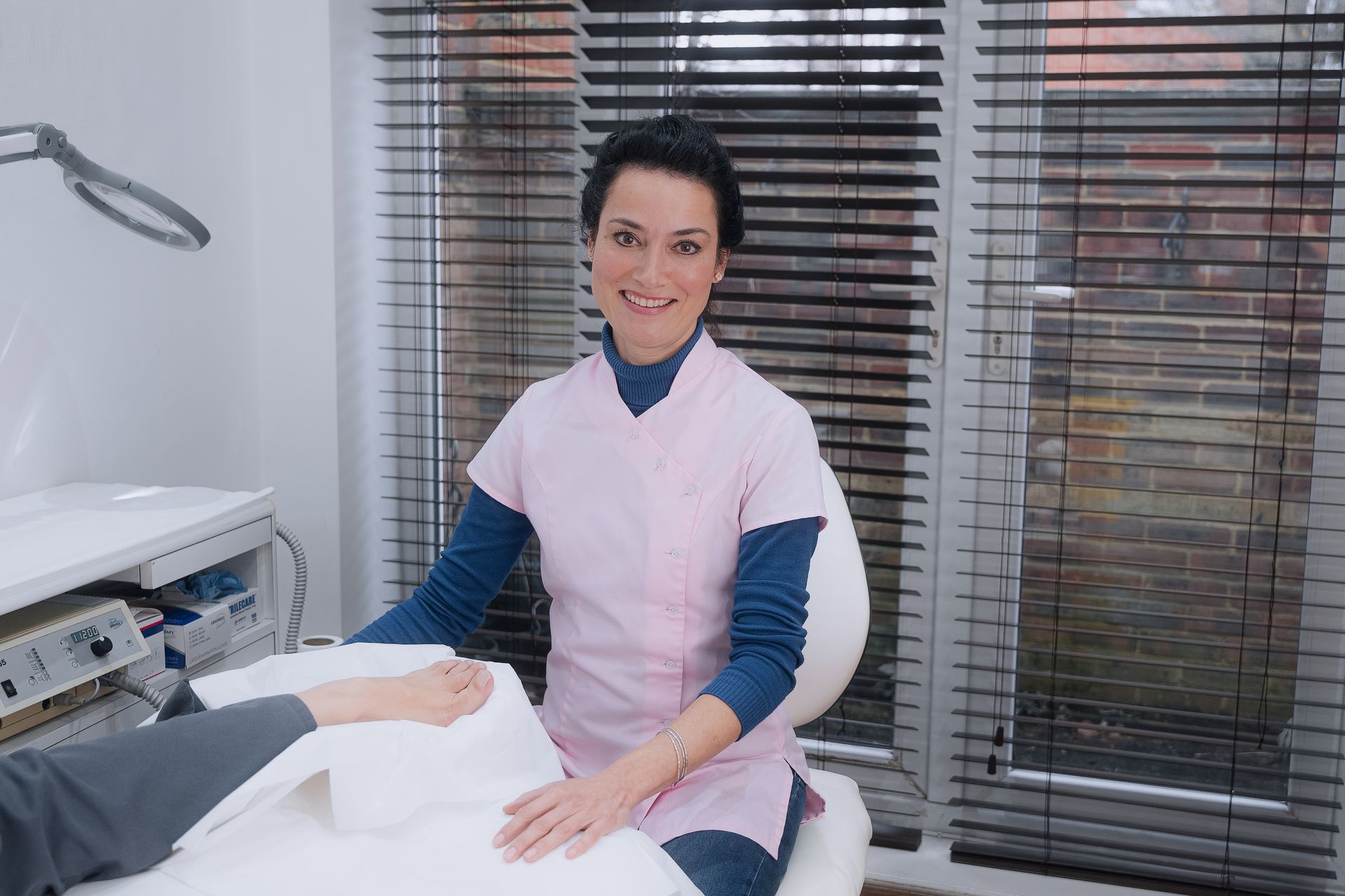 Woman in pink scrubs, assisting patient's foot treatment in clinic.