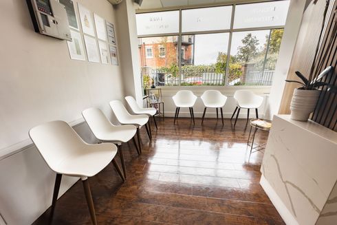 Waiting room with white chairs, window view, and potted plant.