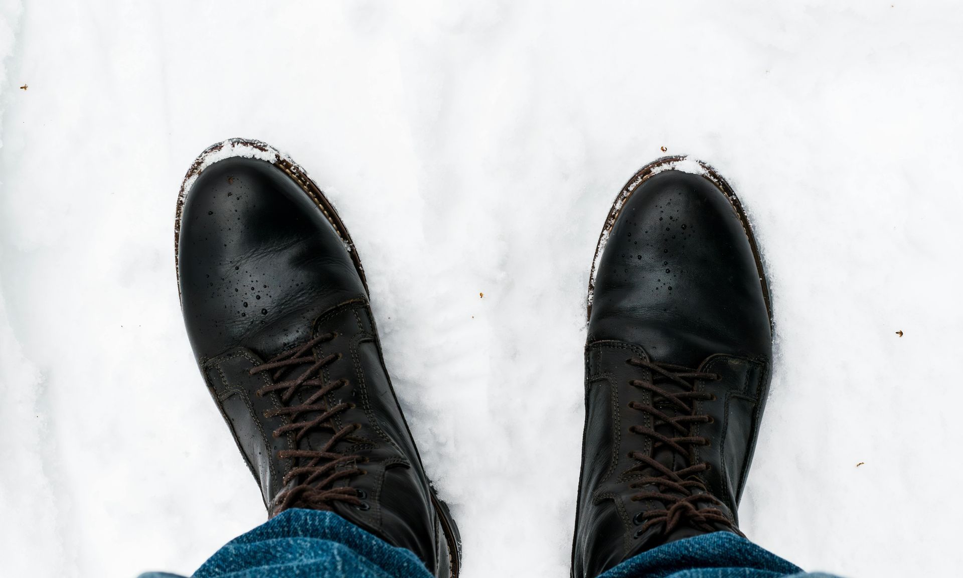 Black leather boots in the snow, viewed from above.