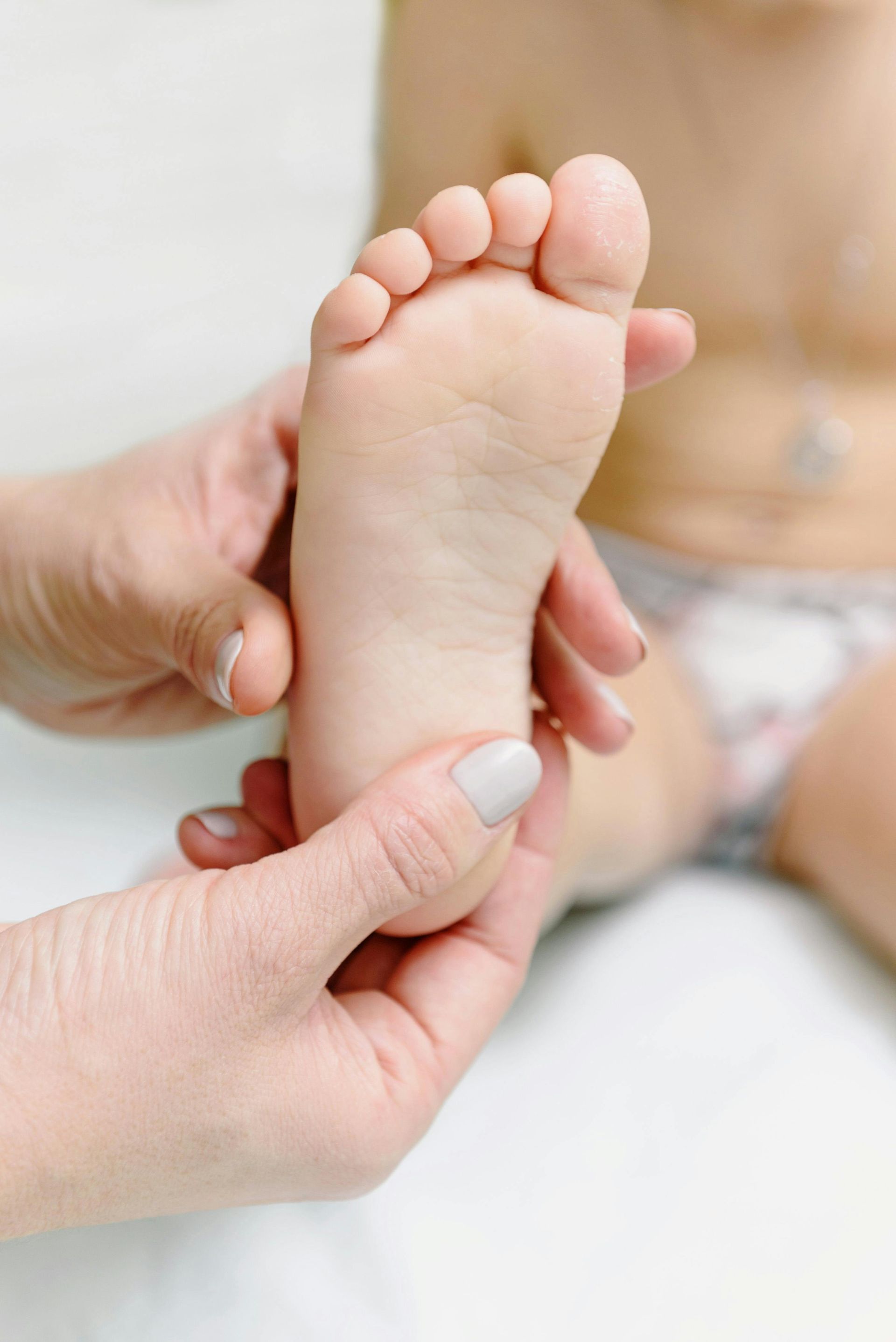 Hands examining a child's foot. The foot is light-skinned, with visible toes.