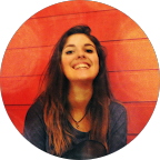 Woman smiling widely in front of a bright orange wooden wall.