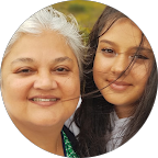 Woman with gray hair smiles next to a young person with long hair. Outdoors.