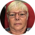 Person with short blonde hair and glasses, sitting in front of a red background.