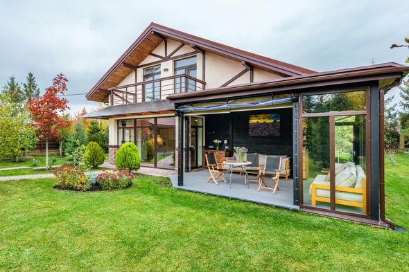 Modern house with a glass sunroom and patio furniture beside a green lawn