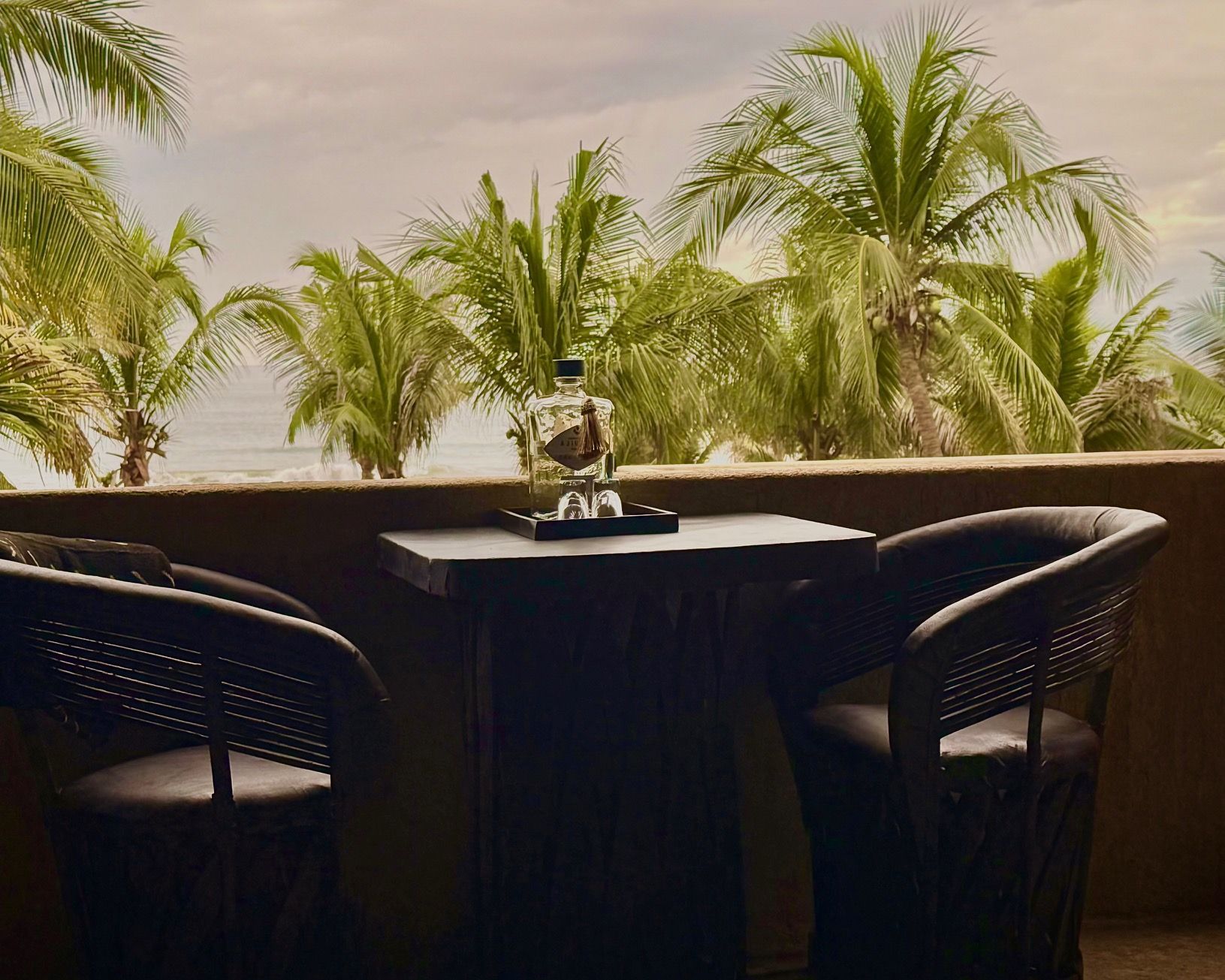 Two chairs and a table on a balcony with palm trees in the background.