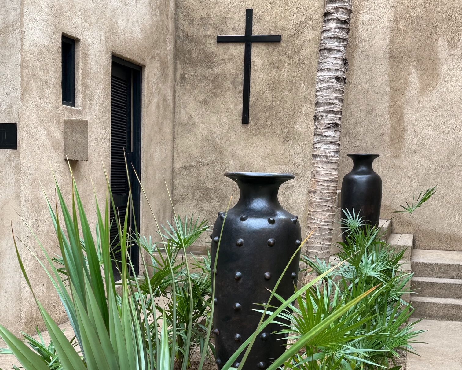 Two black vases are in front of a wall with a cross on it