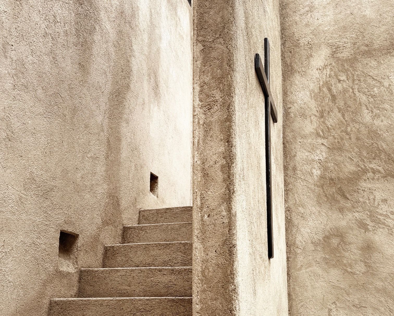 A narrow staircase with a metal railing and a cross on the wall