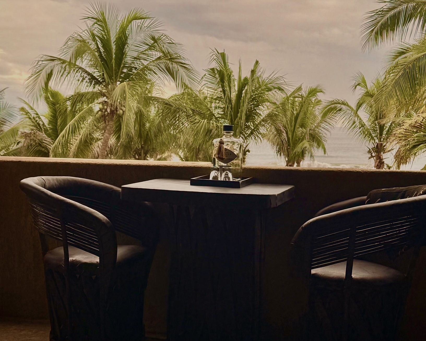 Two chairs and a table on a balcony with palm trees in the background