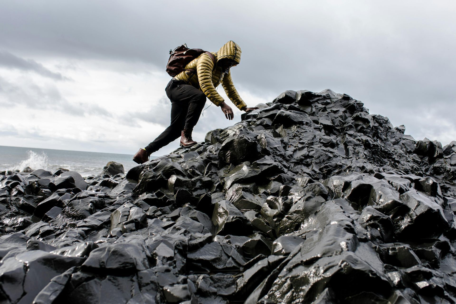 A person is climbing up a rocky hill near the ocean.