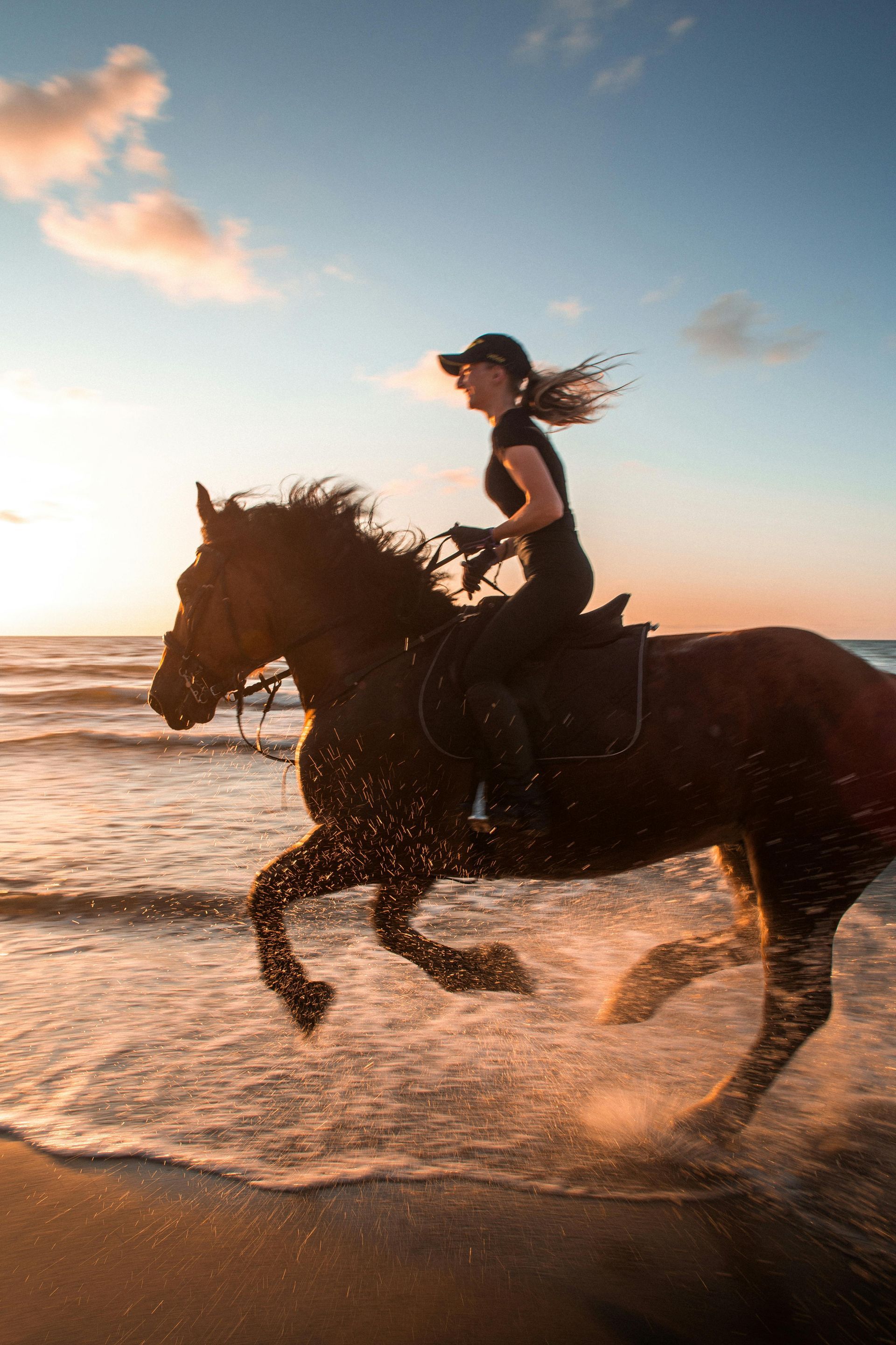 A woman is riding a horse on the beach at sunset.