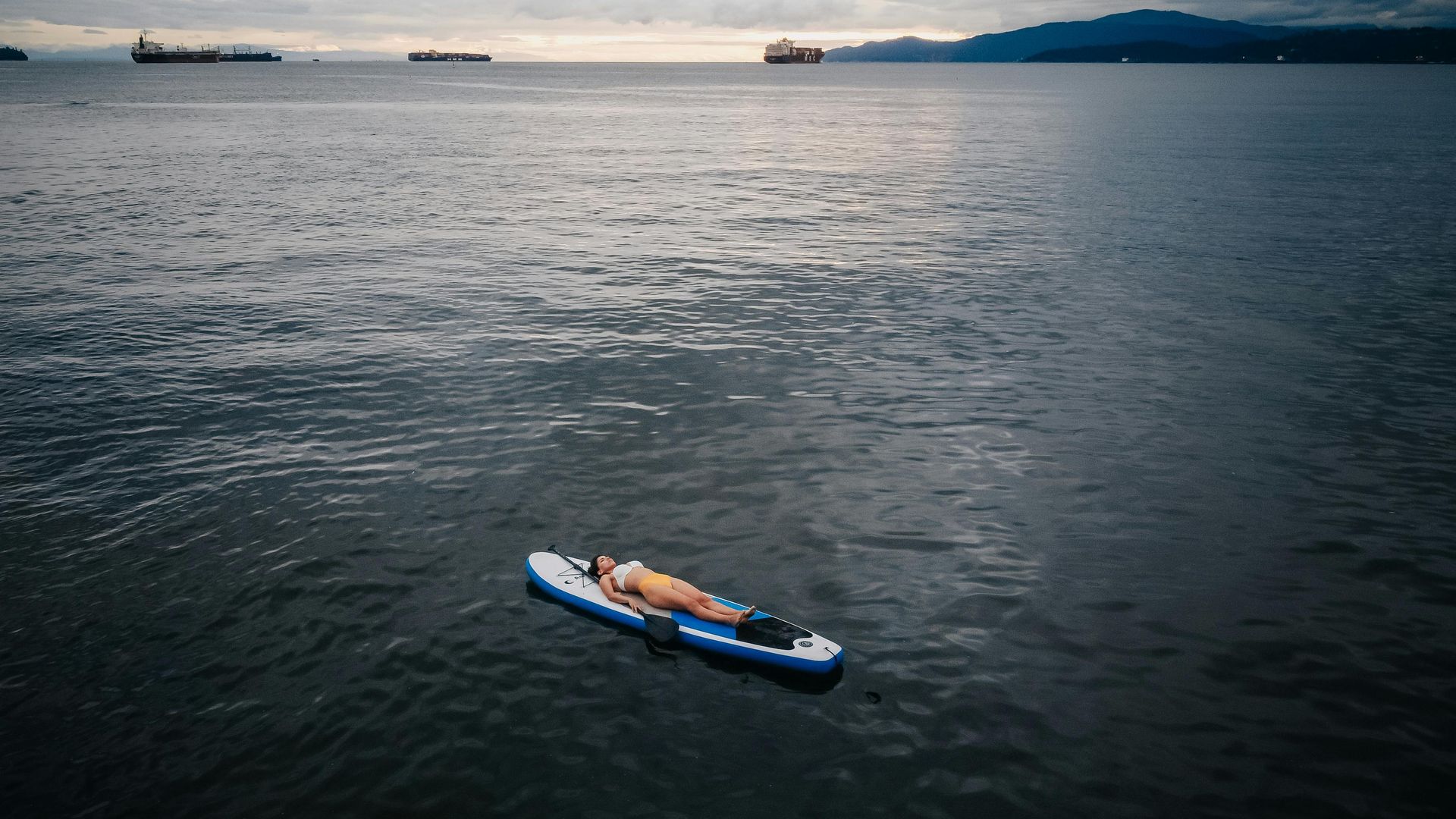 A person is laying on a paddle board in the ocean.