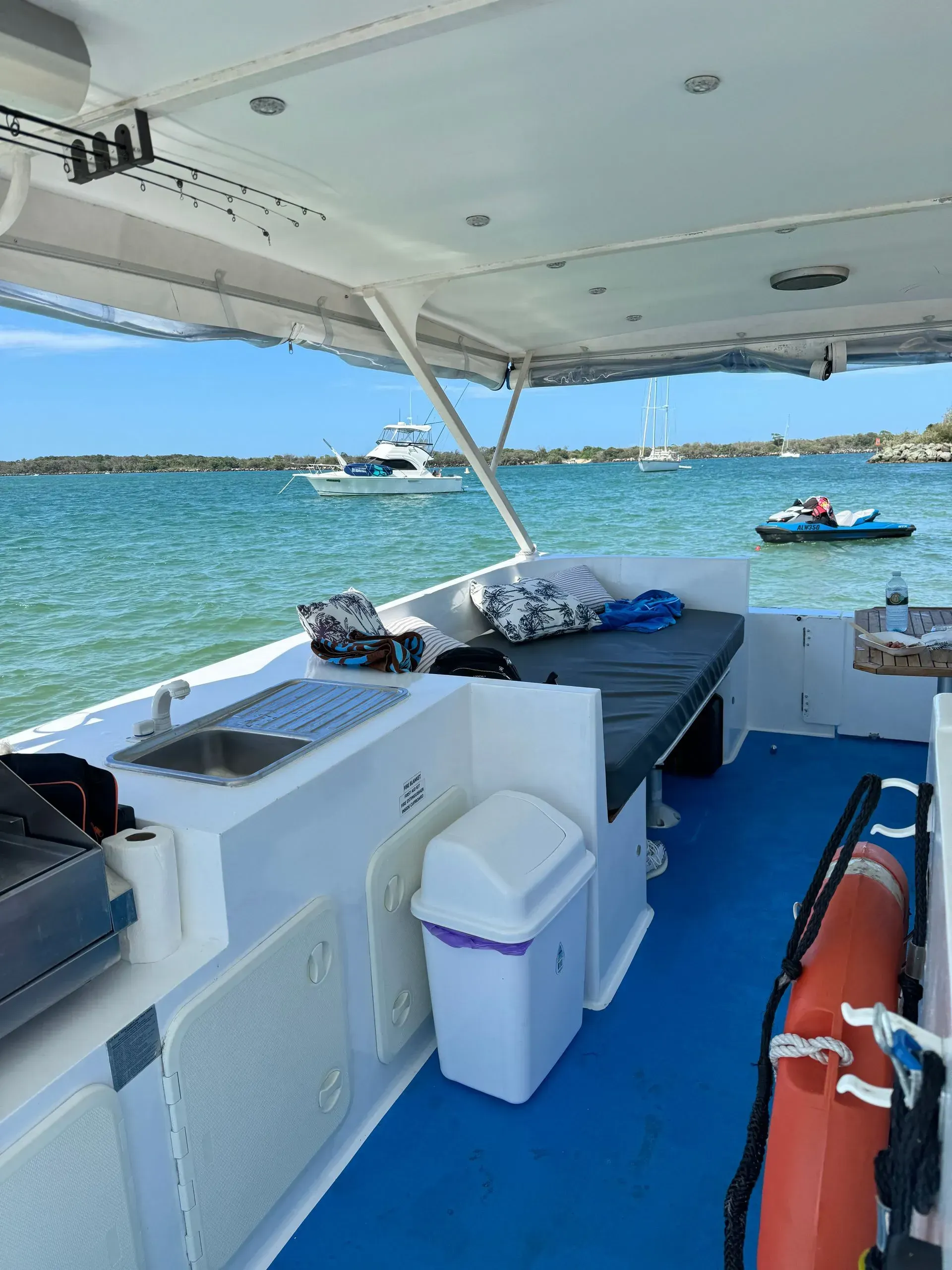 Boat interior, blue deck, sink, trash, cushions, ocean view.