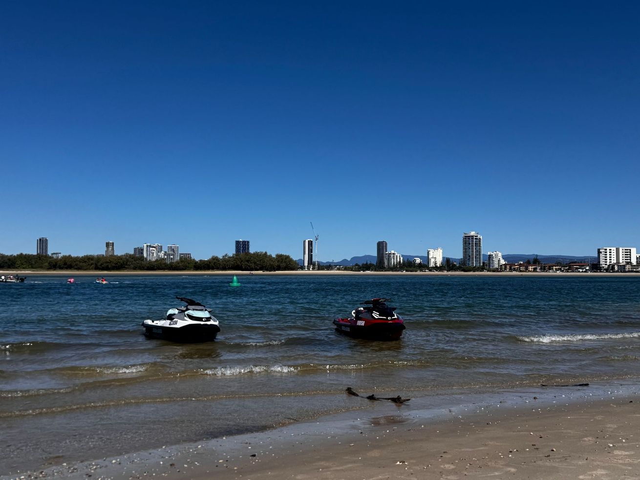 Two jet skis are sitting on the beach near the water.