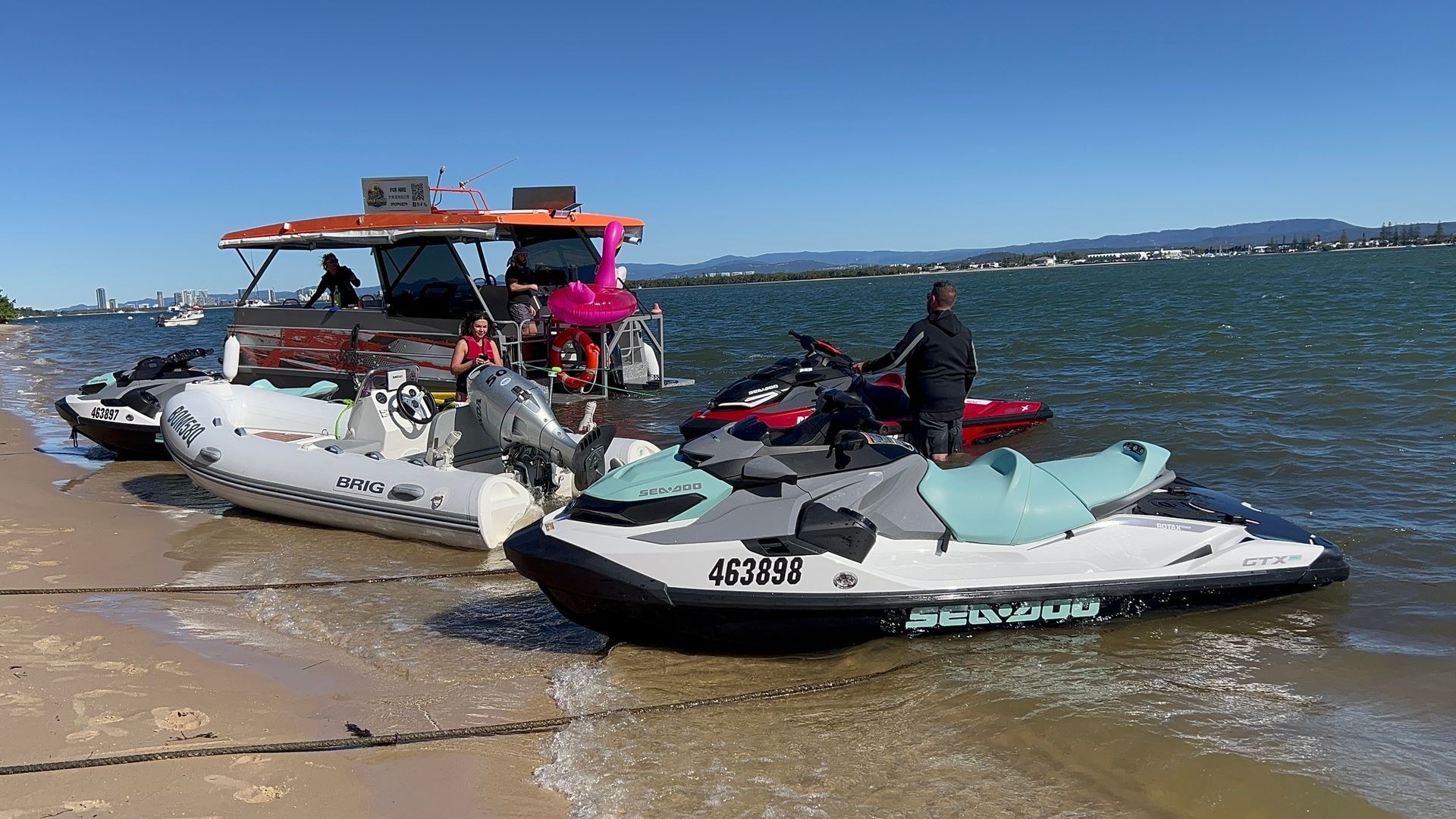 A group of jet skis are parked on the beach next to a boat.