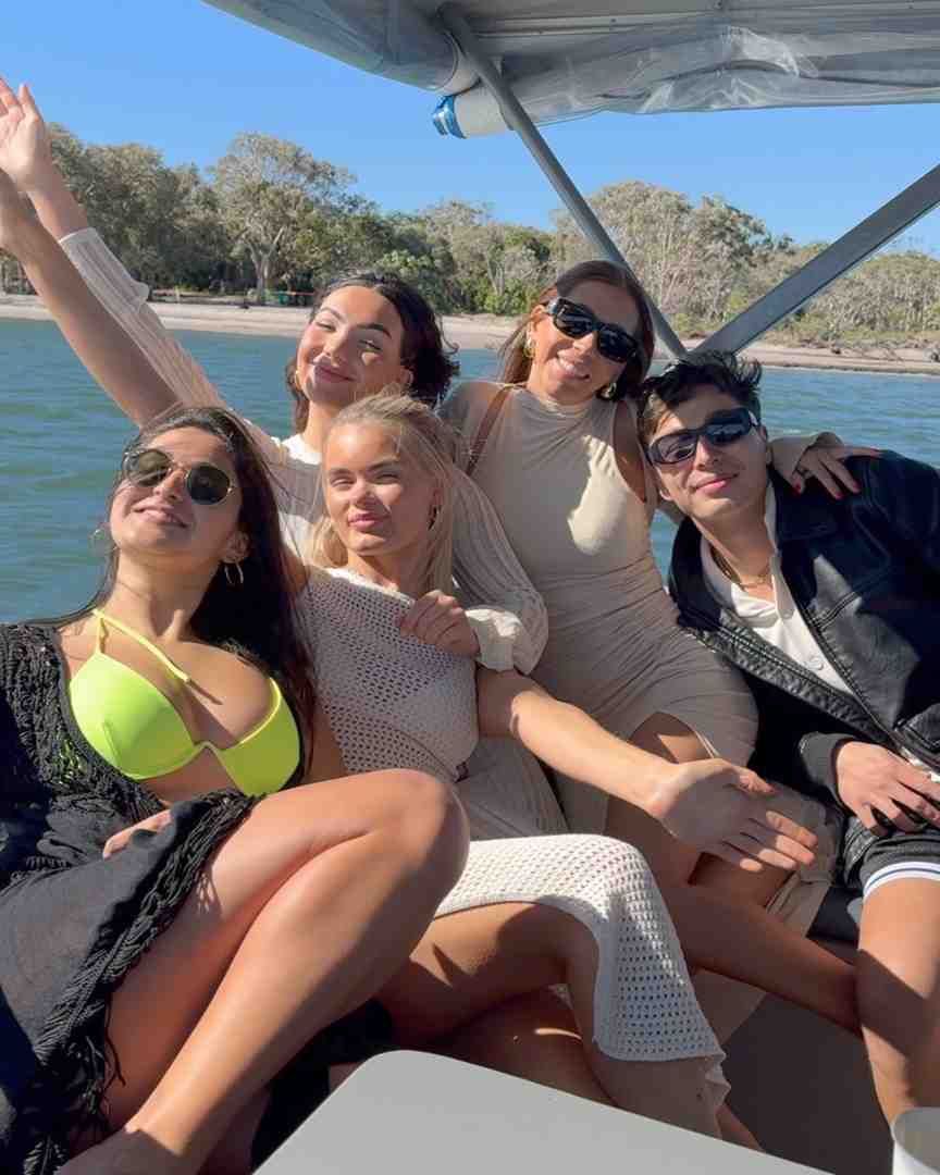 Group of six people on a boat, smiling and posing in the sun.