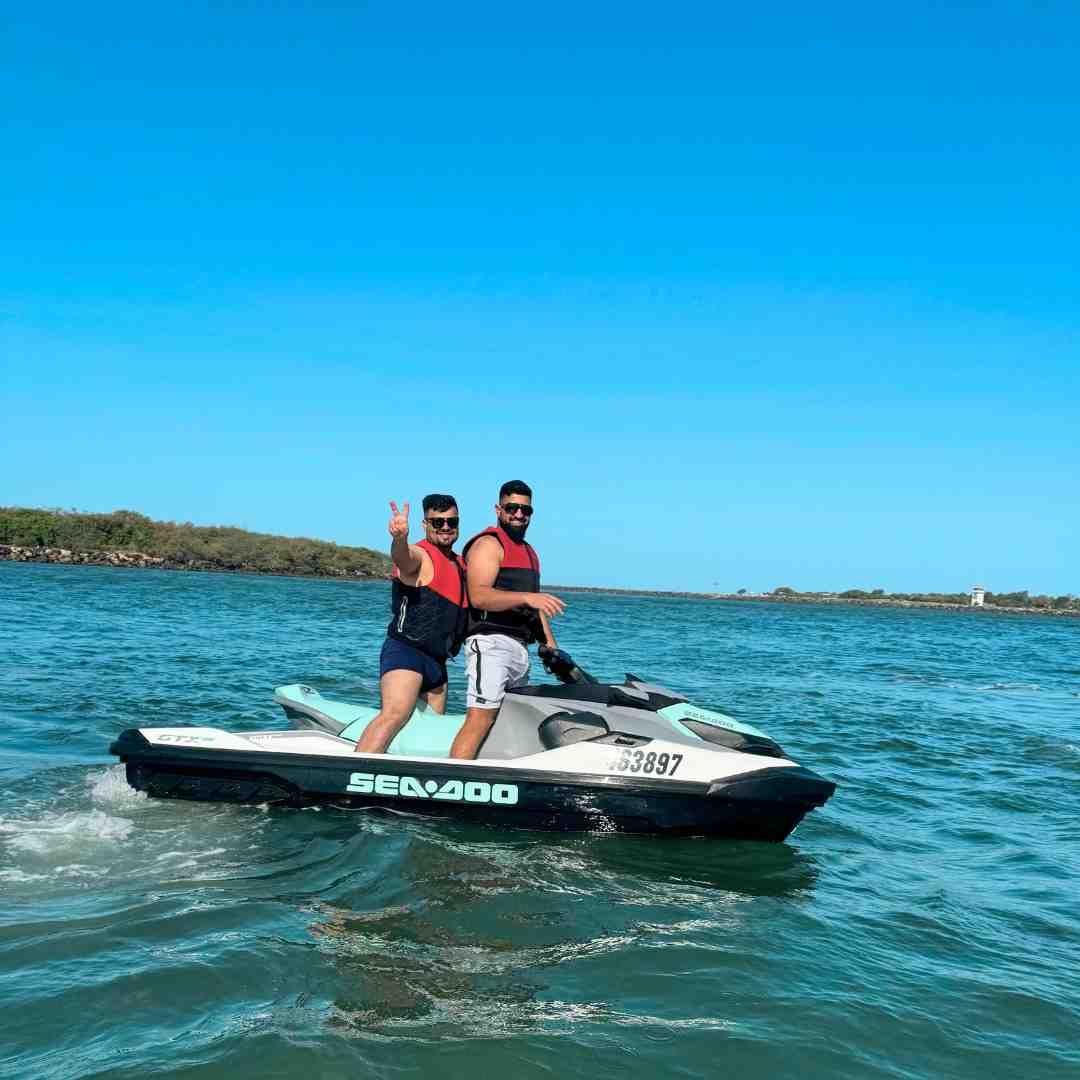 Two men on a Sea-Doo jet ski on a sunny day, one giving a thumbs-up.
