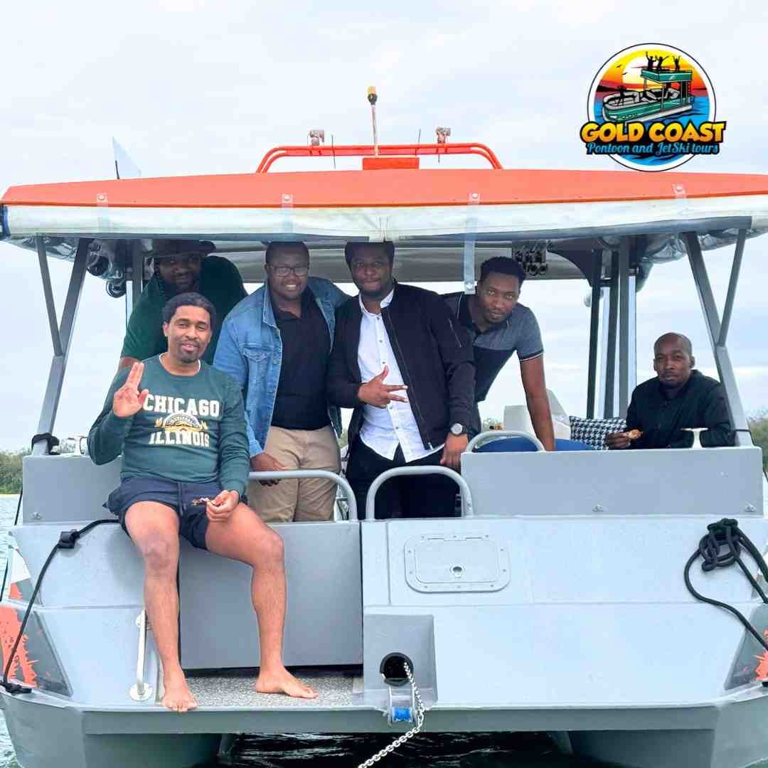 Group of men on a boat on the Gold Coast. One waves, others smile. Cloudy sky.