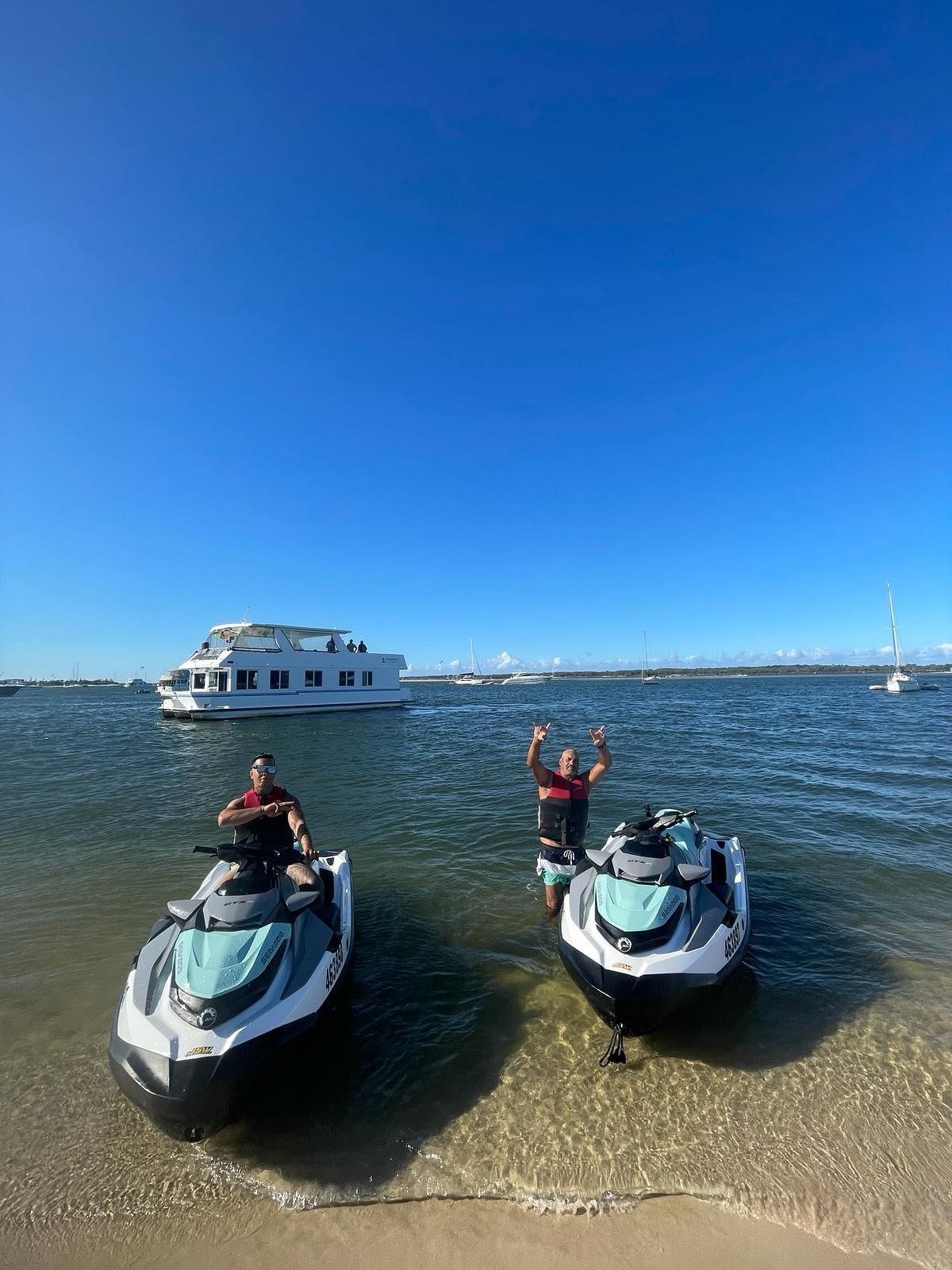 Two people are standing on a beach next to jet skis.