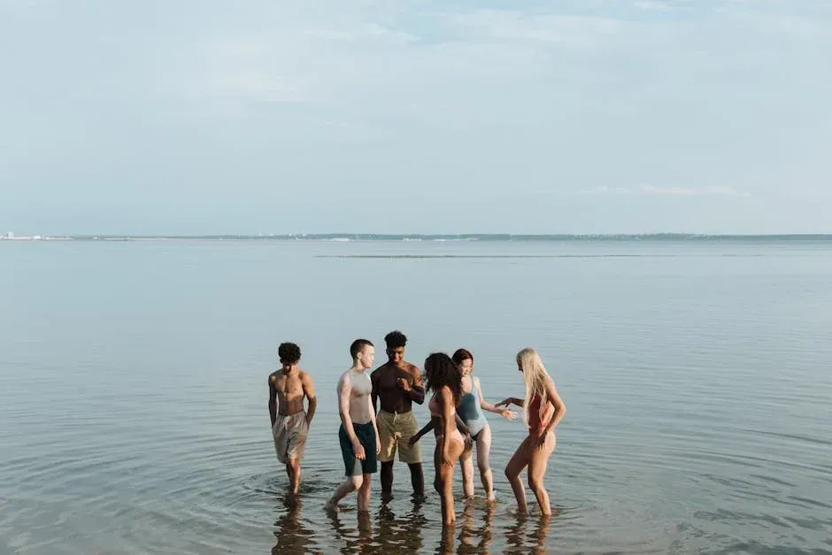 A diverse group of people standing in shallow ocean water, smiling, enjoying a beach day.