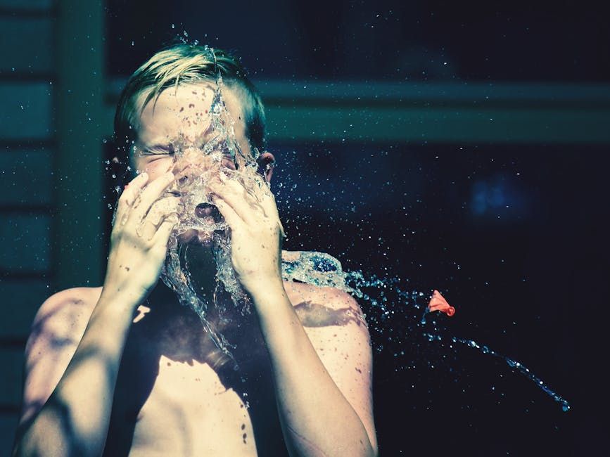 Boy getting splashed in the face with water outdoors, eyes shut, droplets everywhere.