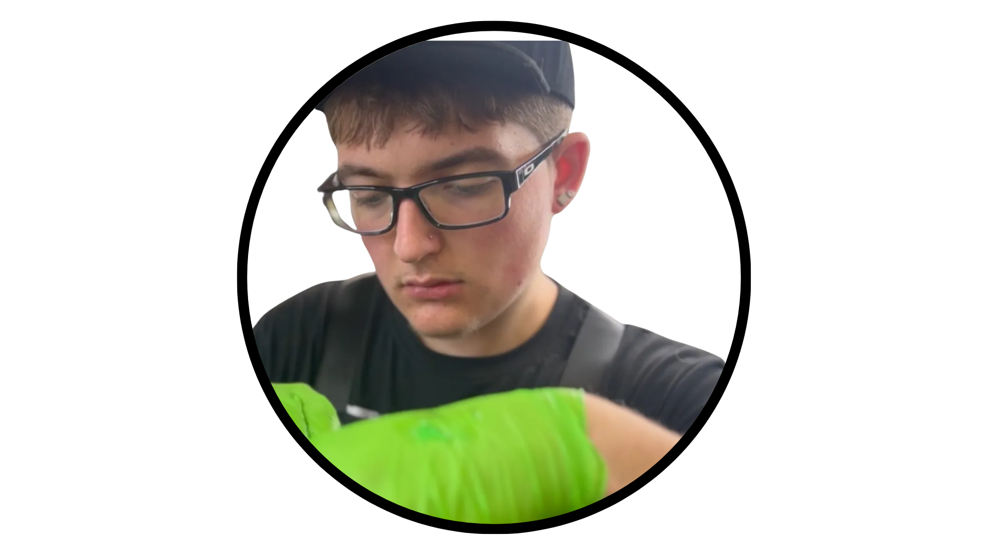 A person wearing glasses and bright green gloves working on a task, framed within a circular border.