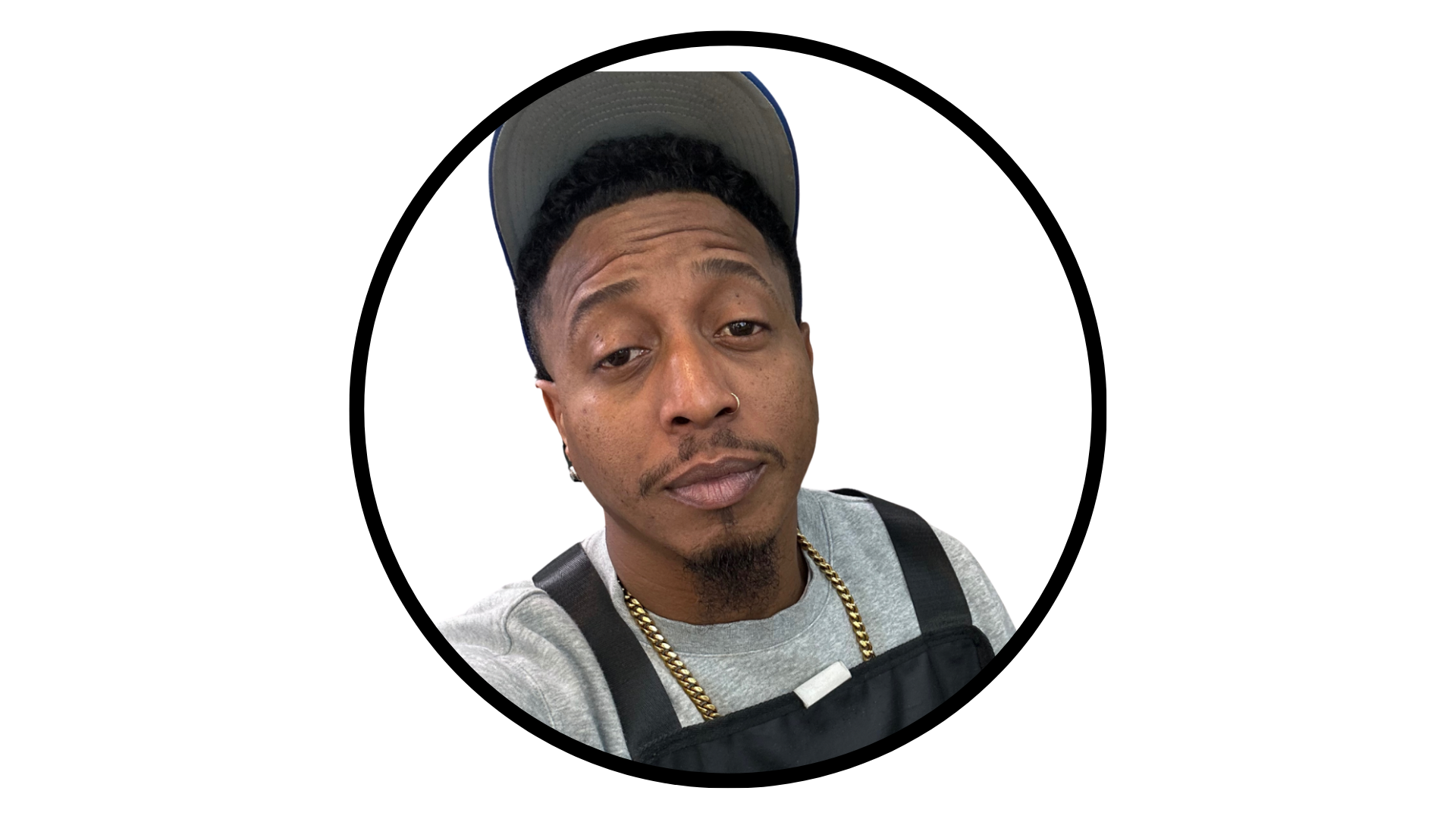 A person wearing a grey cap, light grey sweater, and gold chain, shown from the chest up within a circular frame.