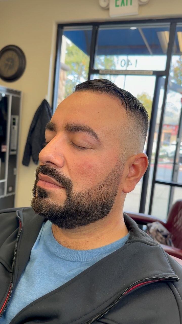 A side-profile view of a person with a fresh fade haircut and groomed beard in a barbershop.