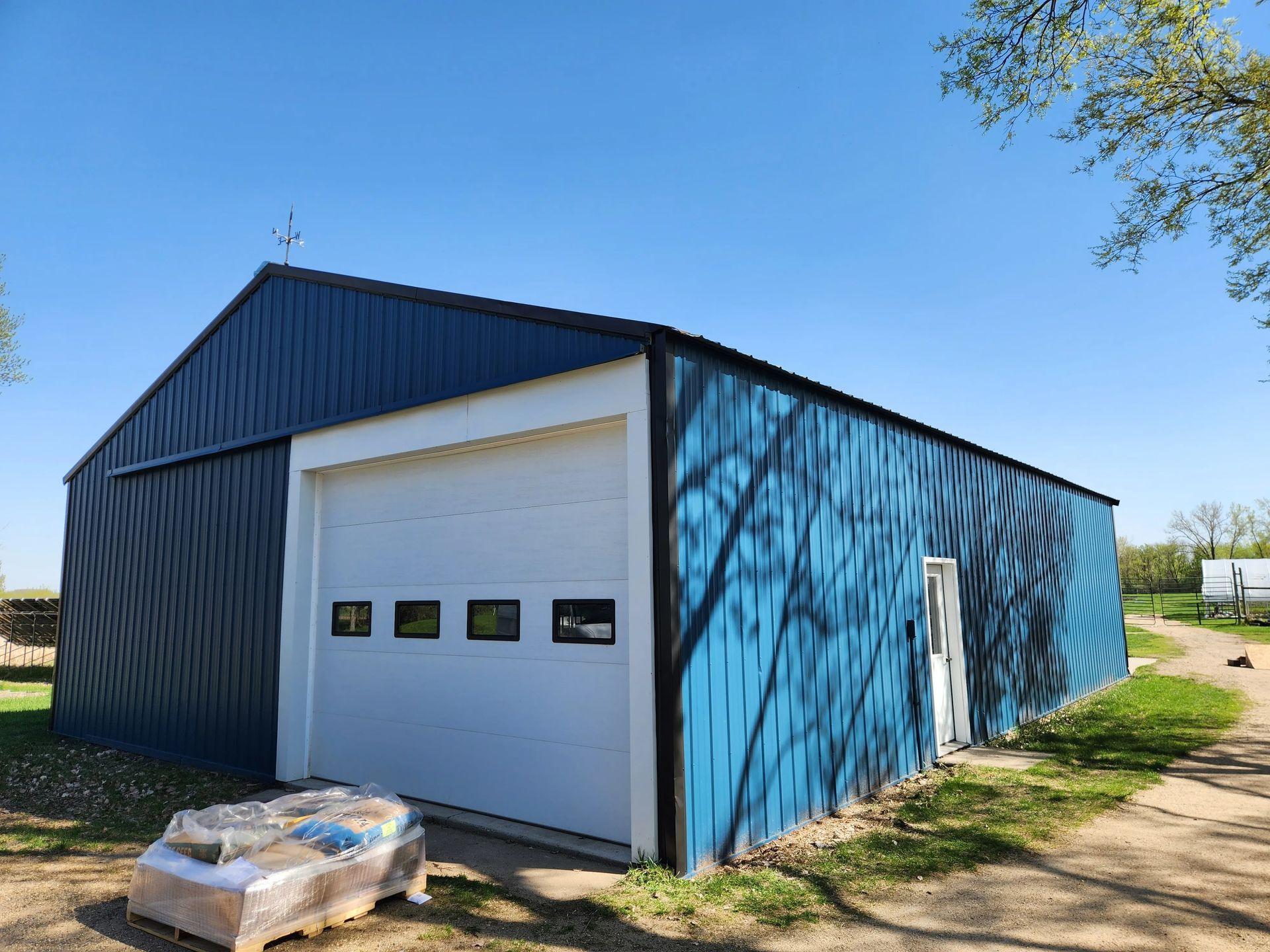 Blue metal shed with a white garage door under a clear blue sky.