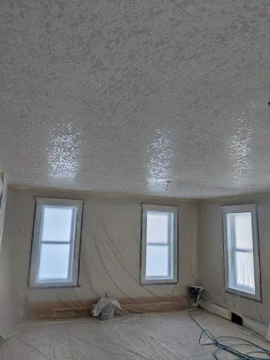 Room with three windows, textured white ceiling, walls, windows covered in plastic, construction.