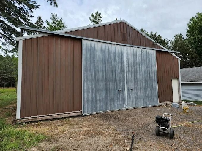 Brown metal barn with large gray sliding doors; a pressure washer sits nearby.