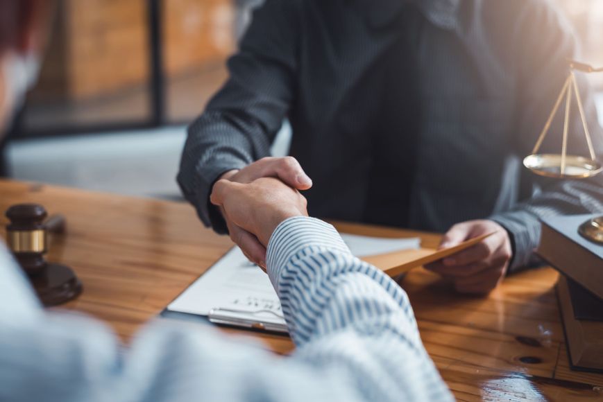 A man is shaking hands with another man while sitting at a table.