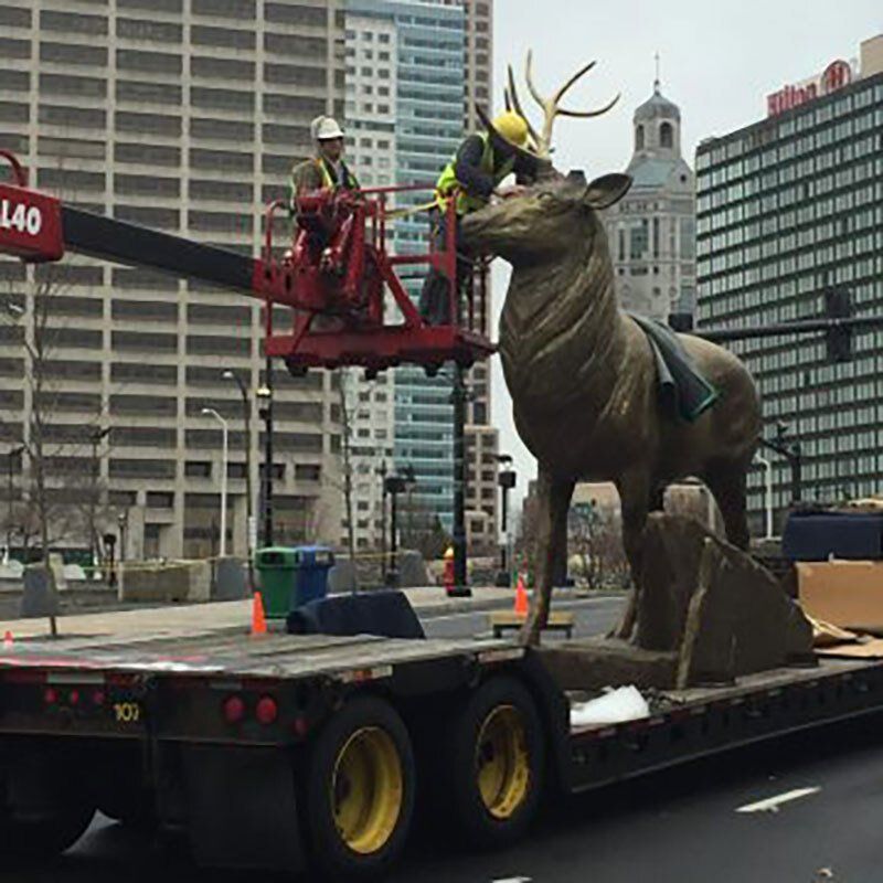 A statue of a deer is being lifted by a crane
