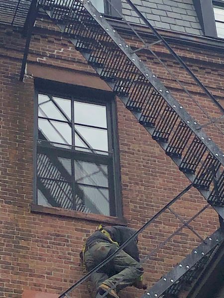 A man is climbing up a fire escape on a brick building